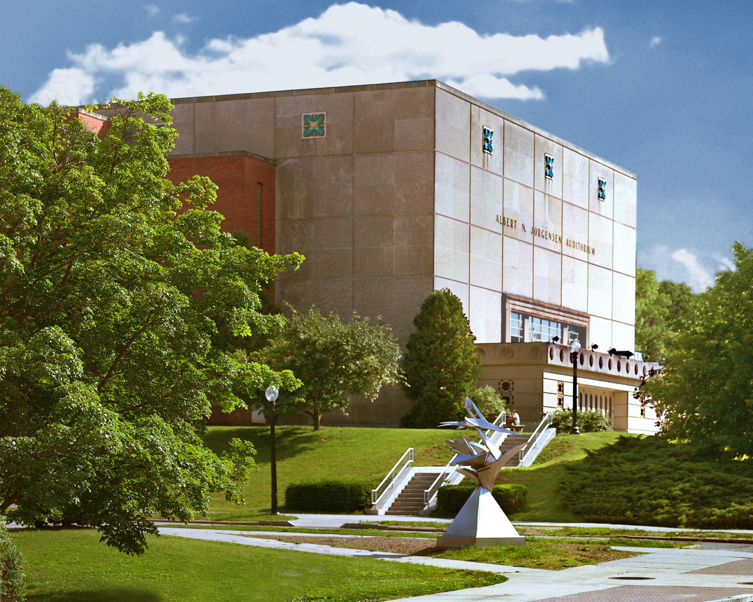 Exterior of the Jorgensen Center for the Performing Arts with trees, lawn, and sculpture on a sunny day.